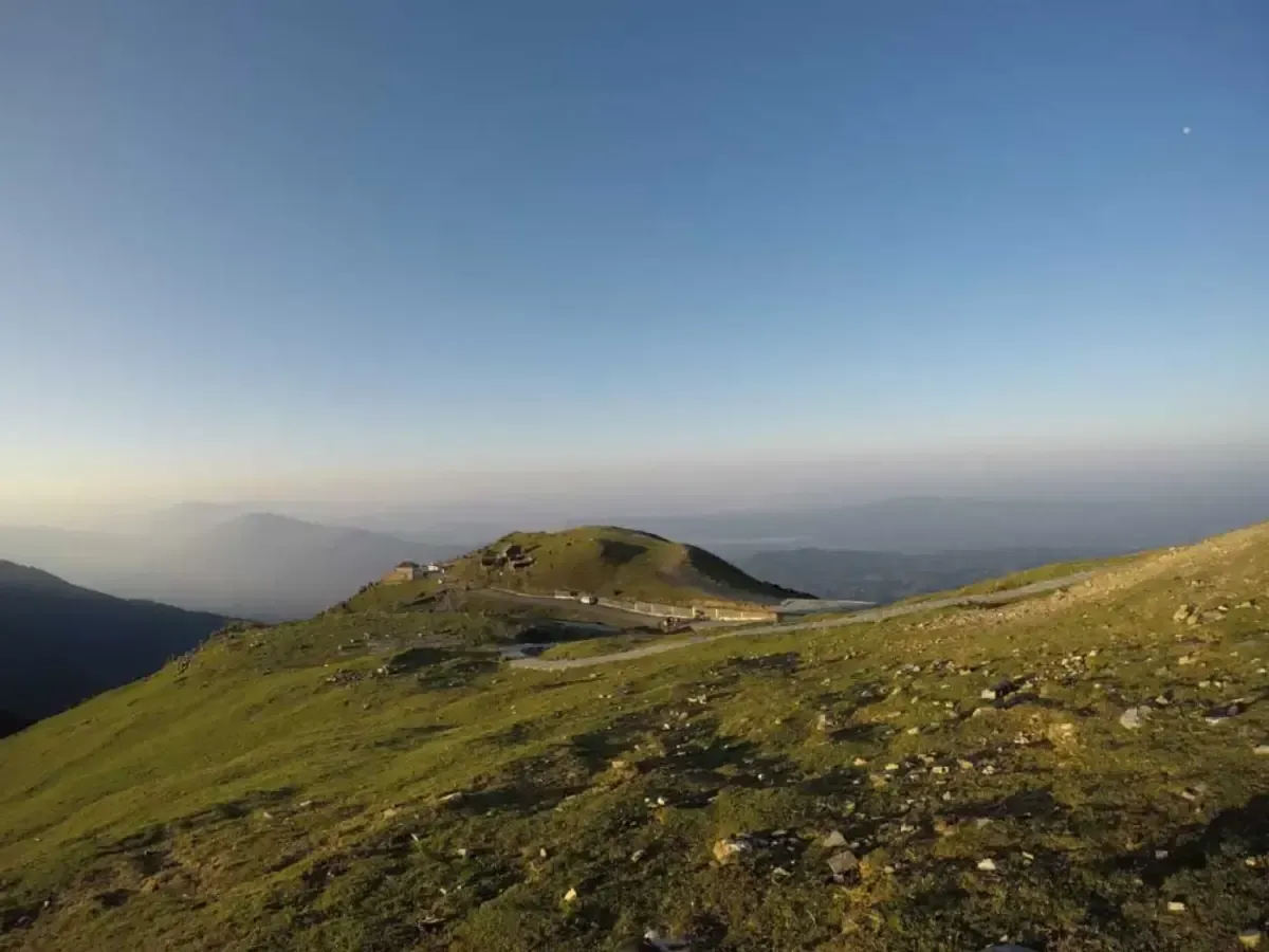 A bare green shoulder of hillside falling away to a hazy plain, the light going behind the ridge