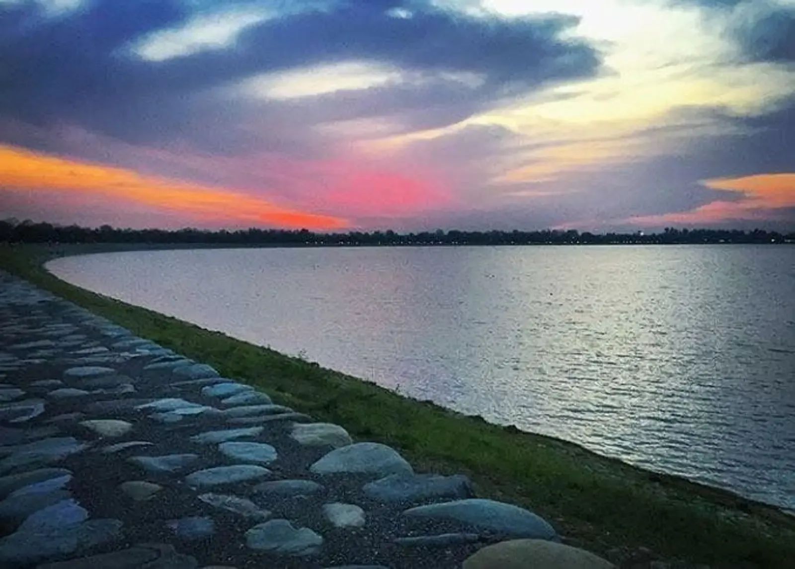 A paved lakeside promenade running out towards still water under a wide sunset sky.
