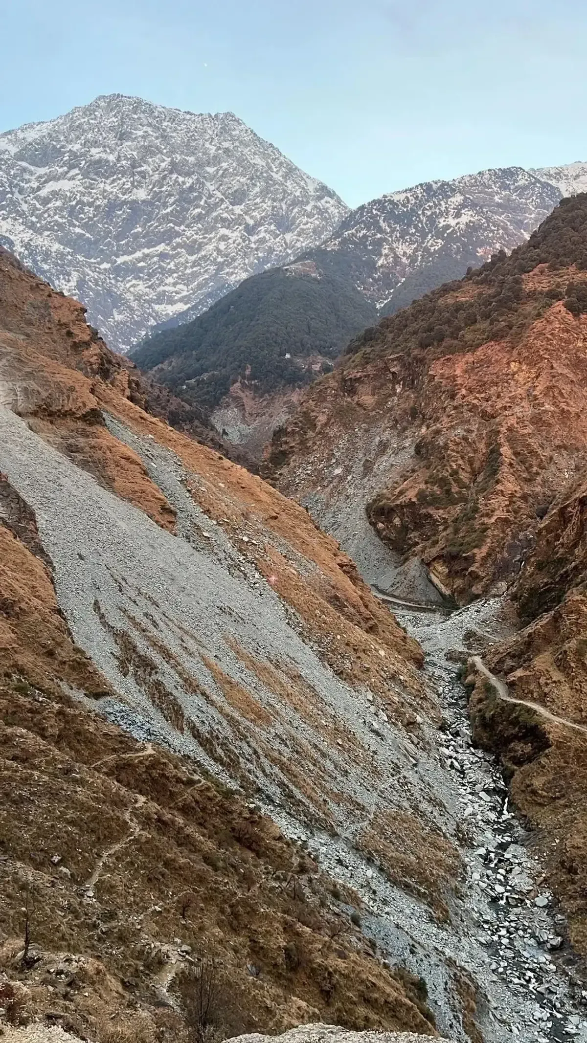 A snow-topped peak standing above a deeply eroded scree slope, a stream running through the boulders at the bottom