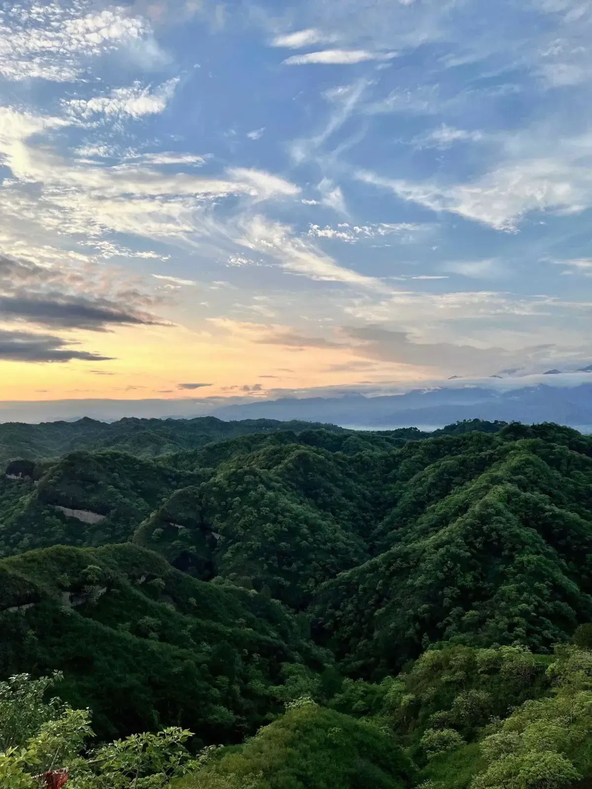 Green forested ridges one behind another under a wide dawn sky, the plain beyond them lost in haze