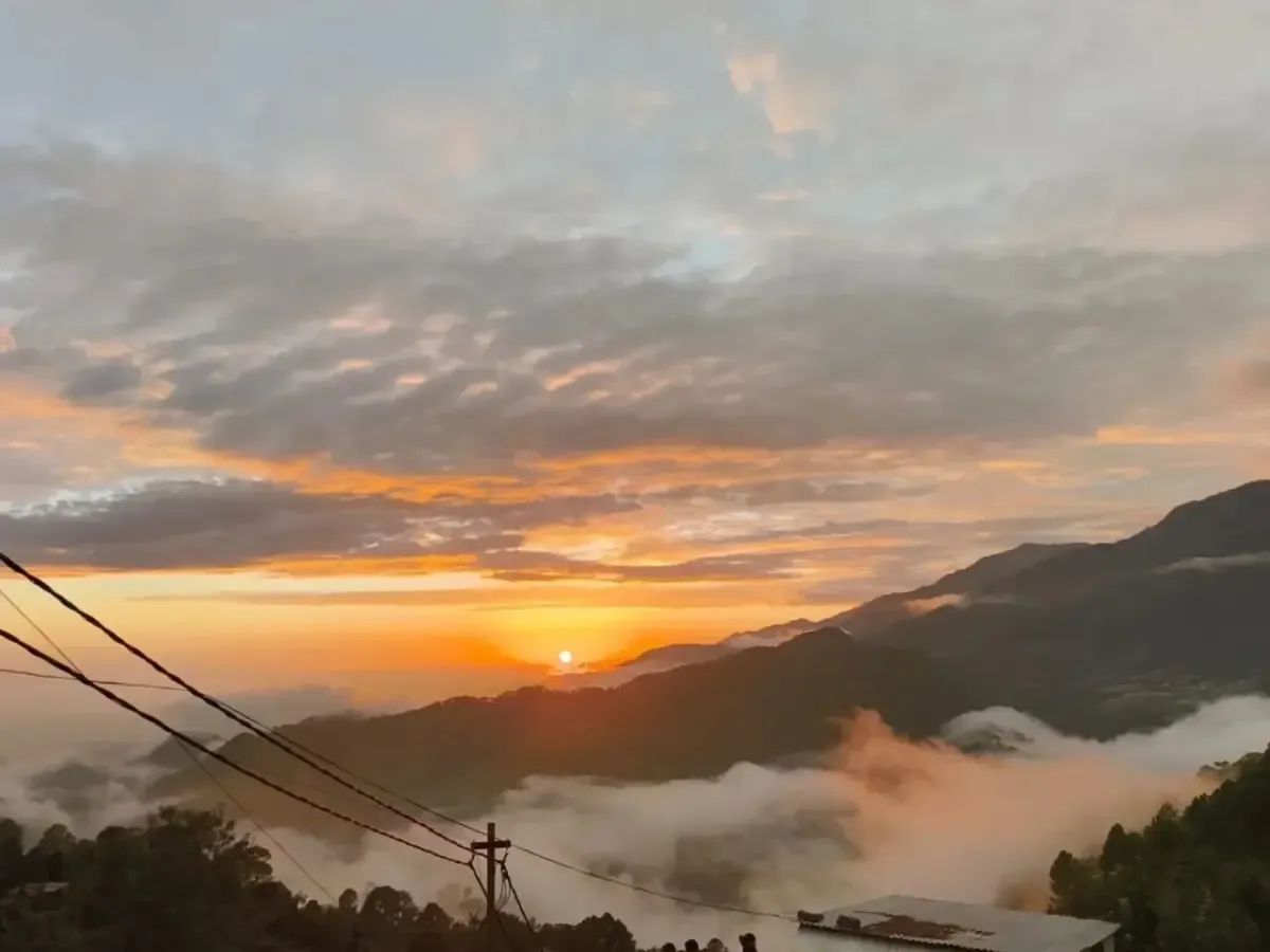 The sun coming up behind a low ridge with cloud lying in the valley below it, the sky orange above and power lines crossing one corner of the frame.