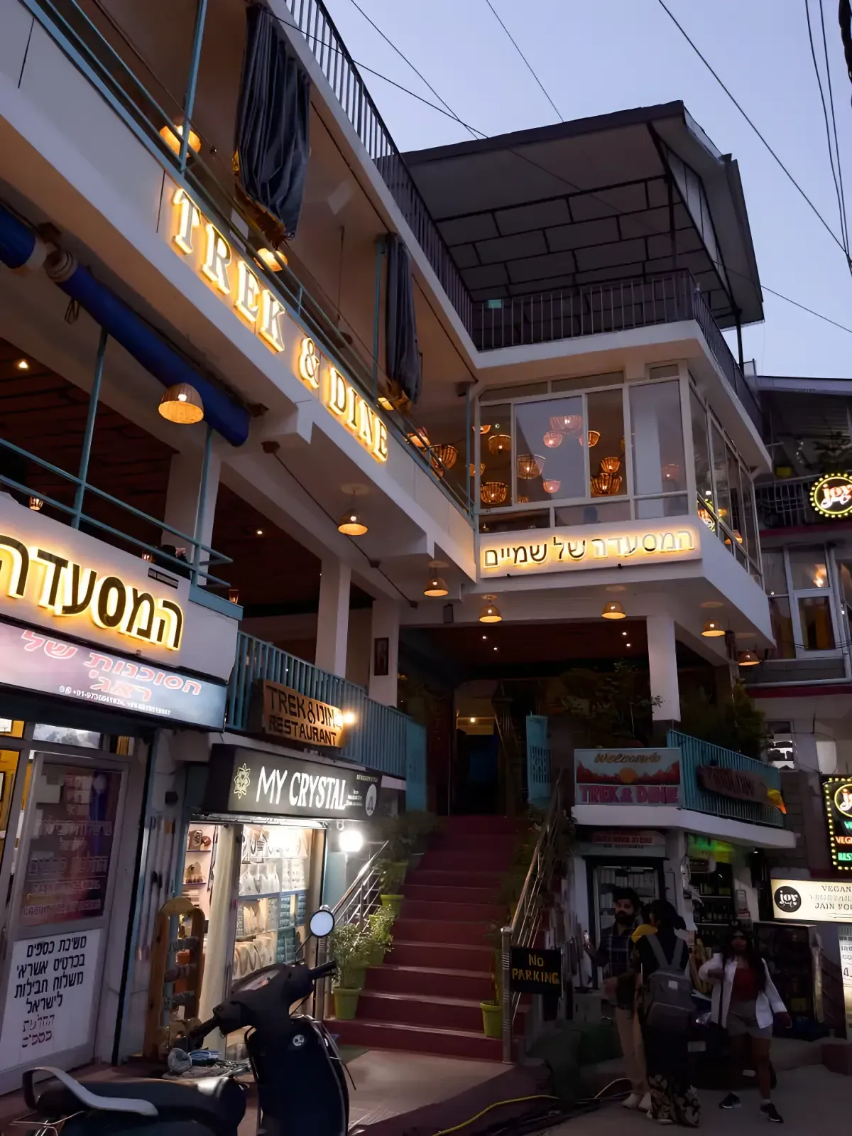 A lit two-storey cafe at dusk, warm light behind its windows and signboards along the balcony