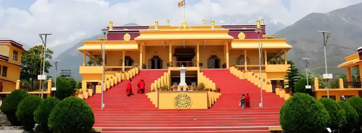 A monastery with a broad red stairway rising to a gold and red facade, figures in maroon robes on the steps