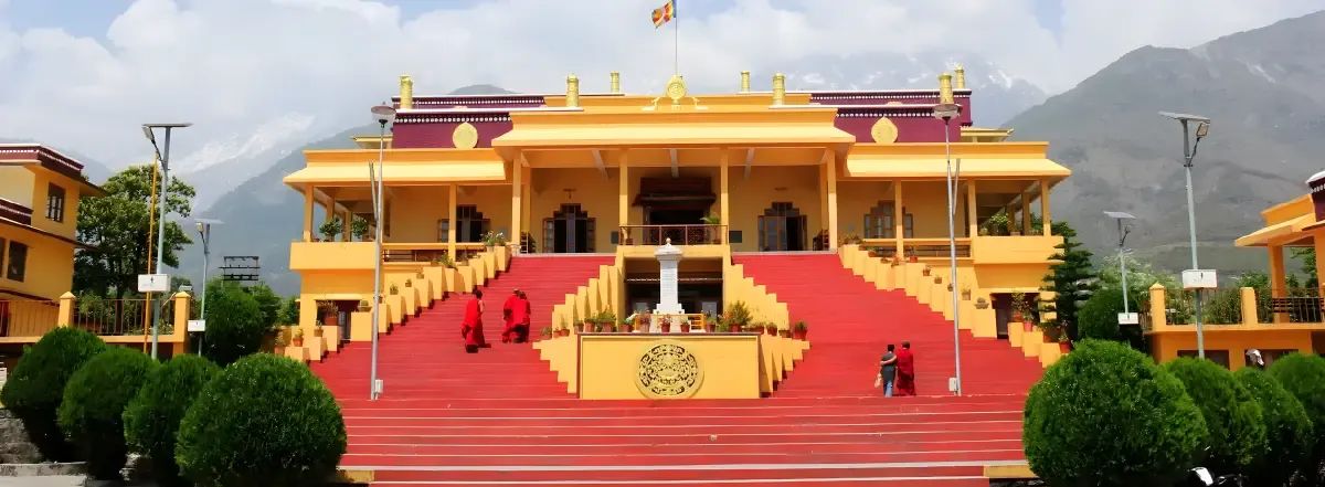 A monastery front painted red, gold and yellow with a broad flight of red steps climbing to the doors, and two figures in maroon robes on the stairs.