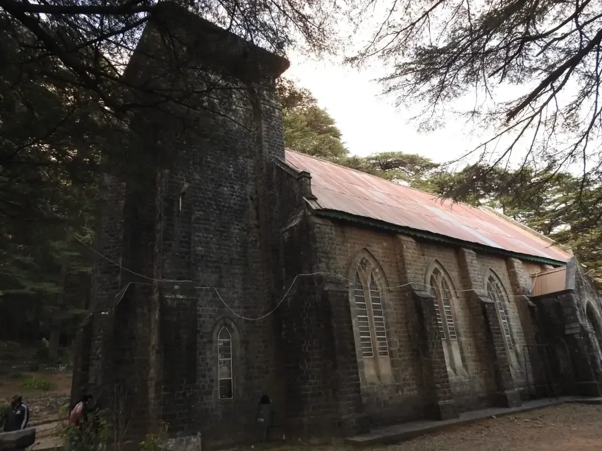A stone church with a steep dark metal roof standing among tall bare-branched trees