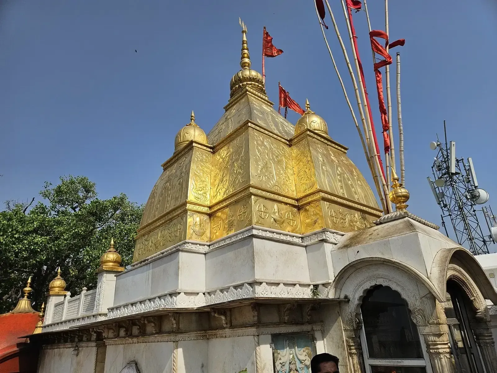 A gold-domed shrine with a tiered spire and red pennants on tall poles, a white archway beside it