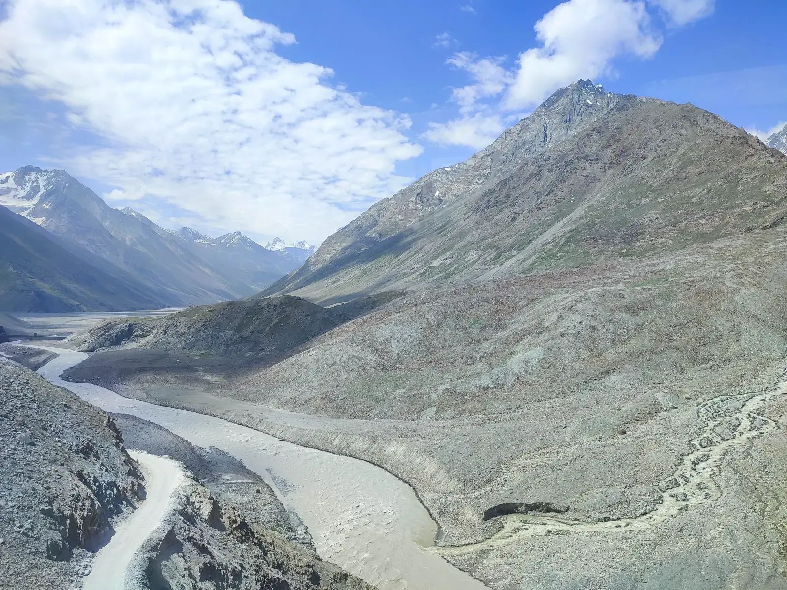 A wide grey valley of scree and old snow opening out under a hard blue sky.