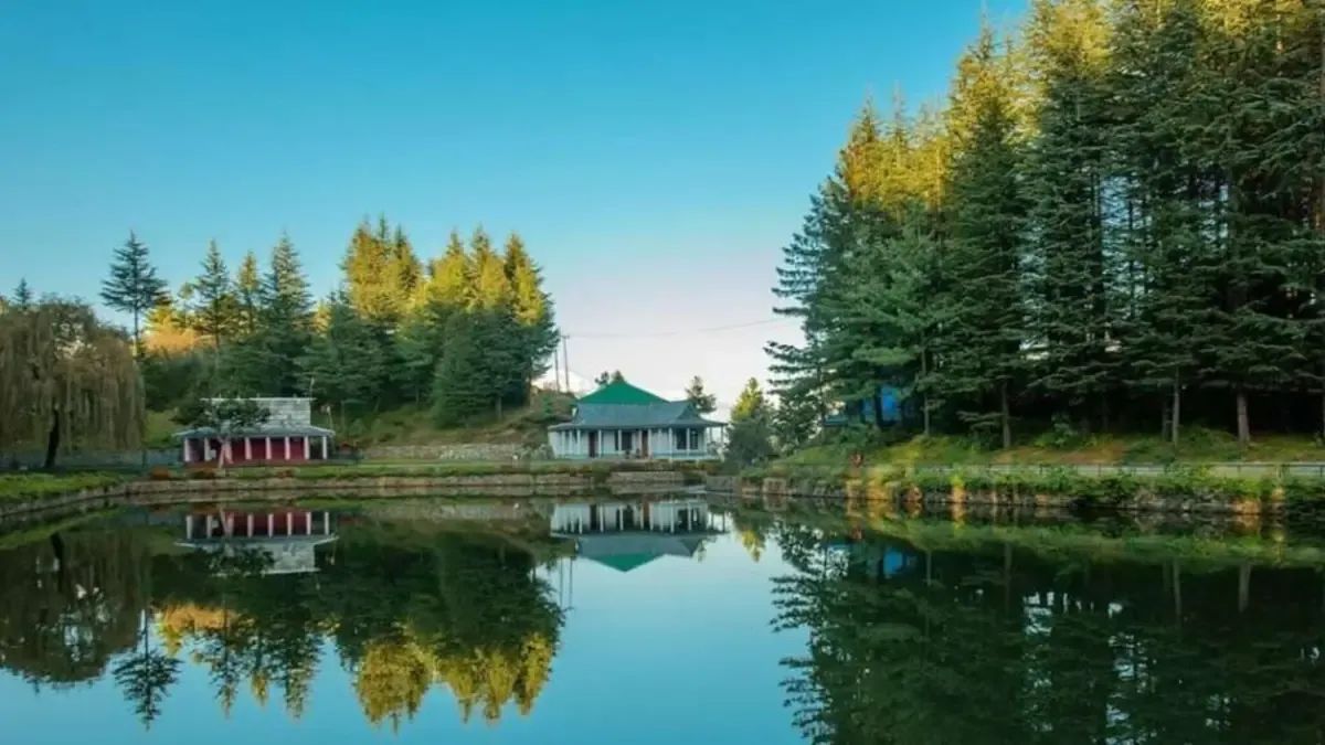 A still lake reflecting the conifers standing around it, with a small green-roofed pavilion on the far bank and deodars closing the view behind.